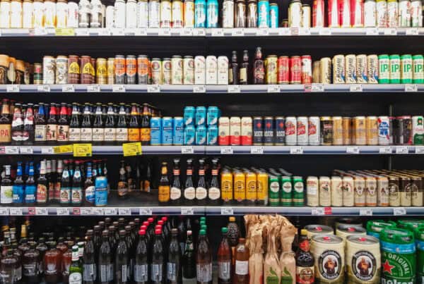 Grocery store beer aisle with rows of beer bottles and cans on shelves.”] ,