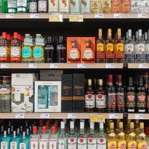 En butikshylla fylld med olika spritsorter i flaskor och presentförpackningar på en utställningshylla i en spritbutik.